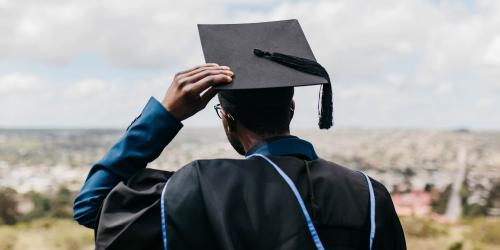 A students in a graduation cap and gown holding onto their cap