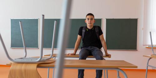 Student sitting on a desk in an empty classroom 