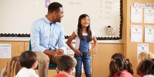 A student standing in front of the class with the teacher next to her