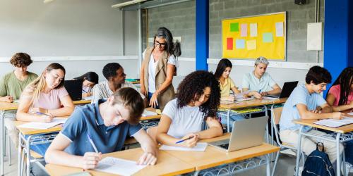 Students working in a classroom with a teacher talking to a student